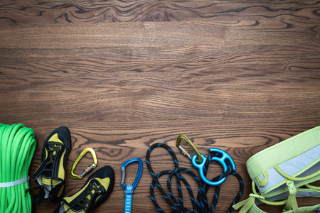 Top view of collection with climbing items, rope, quickdraw, carabiners, harness and shoes on wooden...