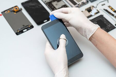 Cropped view of repairman in gloves using special instrument, changing damaged screen and showing process of mobile phone repair in service centerの写真素材