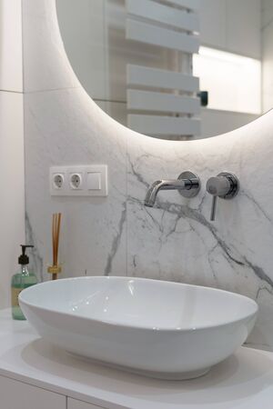 Vertical photo of modern, ceramic wash basin with white water tap in new contemporary bathroom, soap and decor on contemporary table under mirrorの写真素材