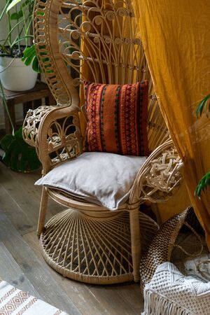 Vertical photo of elegant and comfort room with boho style interior, wicker chair, pillows, cushions and wooden floorの写真素材