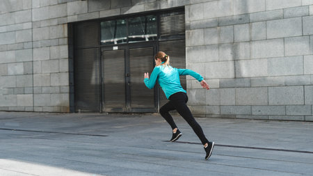 Back view of young adult woman in sportswear and sneakers shoes warming up, running on cardio...