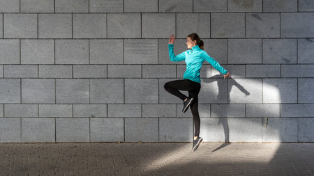 Woman jumping up in cardio workout, against wall with copy space on background. Side view of young...