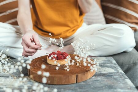 Cropped view of young adult woman decorating sweet cupcake dessert with plants and white flower, creating media content for blogの写真素材