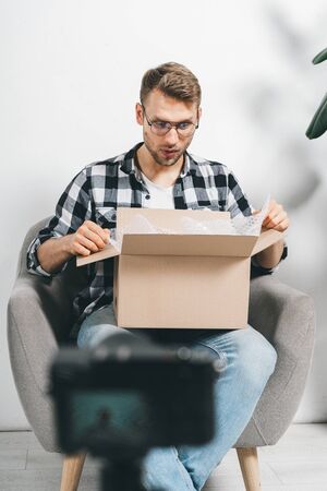 Wondered and happy young adult popular blogger recording video for social media, unpacking carton box, using modern broadcast equipment, sitting in studioの写真素材