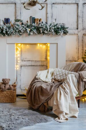 Cozy living room with winter style interior, garland lights over fireplace, plaids on comfort armchair, rug and traditional december decor at homeの写真素材