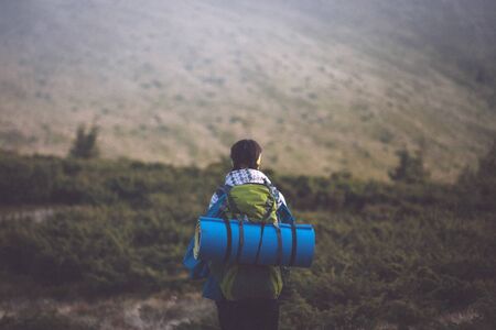 Back view of young adult woman with backpack looking at scenic nature landscape in mountainの写真素材