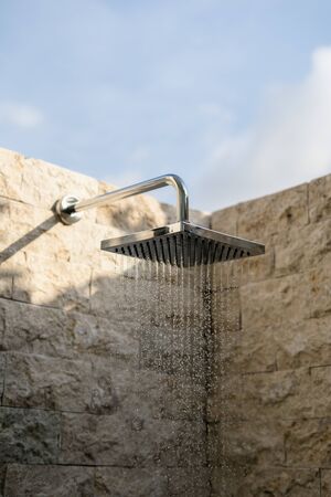 Vertical photo of close up of water flowing from turned on shower head in modern bathroom interiorの写真素材