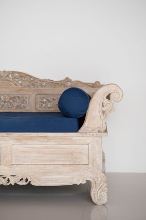 Carved and wooden sofa with blue cushion near white wall with copy space in stylish traditional interior roomの写真素材