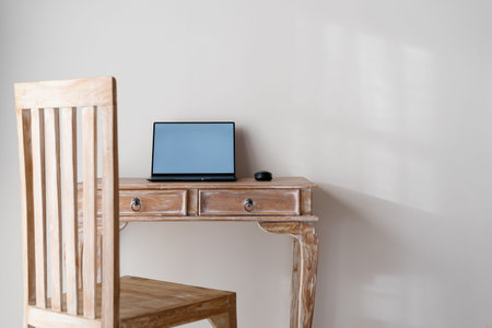 Laptop computer with copy space on display monitor on wooden table in house with chair and white wall in roomの写真素材