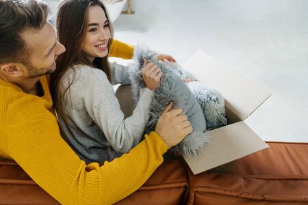 Concept of starting new life. Happy young adult girlfriend and boyfriend move in new rent house together, packing boxes with interior decor, sitting in room with copy space on backgroundの写真素材