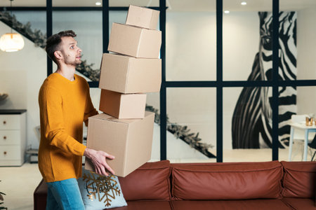 Side view of scared young adult guy move in new flat, dropping pile of boxes from hands, looking how...