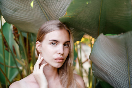 Organic cosmetics concept. Portrait of young adult woman with natural makeup and healthy skin standing in tropical nature with plants on backgroundの写真素材