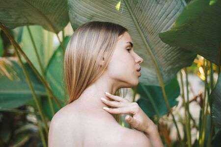 Wellness and bodycare concept. Back view of calm young adult girl with natural makeup and healthy skin standing in tropical nature with plants on backgroundの写真素材