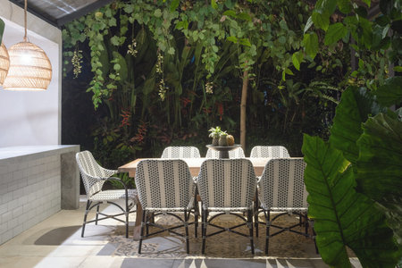 Dining room table and comfortable chairs on open kitchen at evening against green natural background
