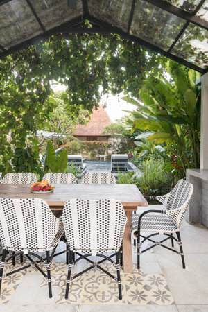 Vertical photo of cozy dining room table and chairs on open kitchen against house and green plants...