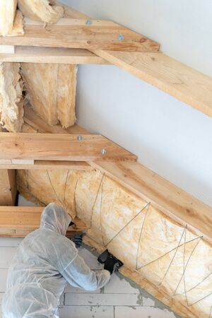 Low angle view of one professional worker in overalls working with rockwool insulation material, standing inside new house under construction, fasten warmth layer on ceiling and wallの写真素材