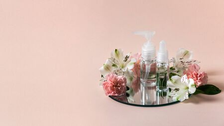 Panoramic view of natural cosmetics product in transparent plastic bottles near flowers isolated on pastel pink background with copy space and mirrorの写真素材