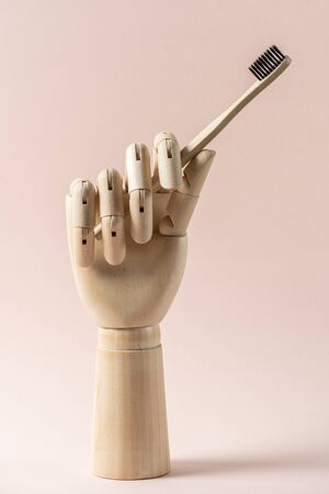 Vertical view of wooden hand holding bamboo toothbrush with eco friendly and recycled material isolated on pastel pink background with copy spaceの写真素材