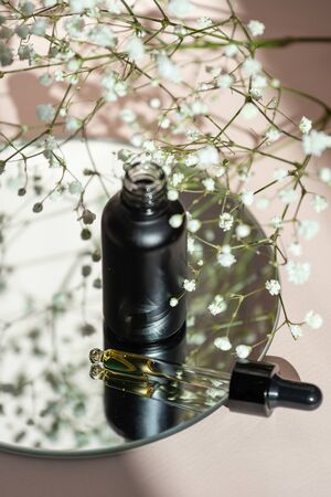 Rejuvenation and facial oils. Vertical view of glass bottle with flowers component in organic cosmetics product in pipette on pastel pink backgroundの写真素材