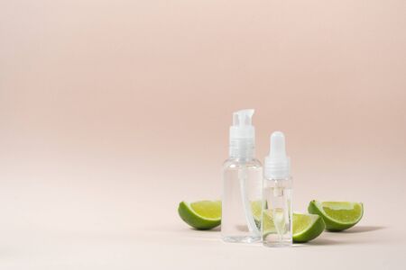 Concept of natural cosmetics product. Transparent bottles with vitamin tonic water and anti aging serum near sliced citrus lime isolated on pastel pink background with copy spaceの写真素材