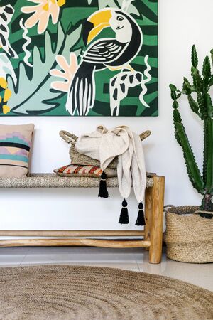 Concept of decor objects at home. Vertical photo of room with contemporary interior design, wooden bench seat, pillows, textile plaid, rug on floor and cactus plant in basketの写真素材