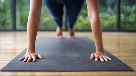 Cropped view and selective focus of young adult athletic woman standing in plank position, making yoga exercise in fitness class, training in sportswear against nature and plants on backgroundの写真素材