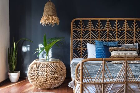 Stylish bedroom interior at modern house with ethnic decor, lamp over bedside table, comfortable wicker headrest at bed and cactus plant in flower potの写真素材