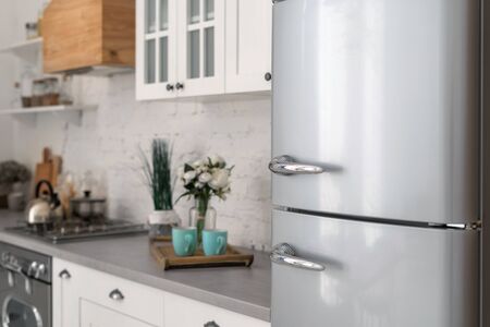 Selective focus on new refrigerator against wooden furniture with cabinets in modern kitchen. Concept of apartment with white interiorの写真素材