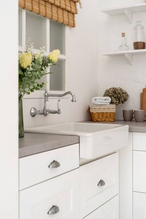 Vertical photo of element in kitchen interior with bright modern style, flowers on countertop and sink next to windowの写真素材