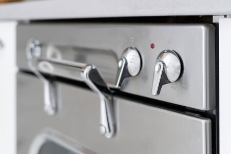 Selective focus on silver metallic switch near handle at modern gas oven. Built in cooking appliance on cozy kitchen at house with modern interiorの写真素材