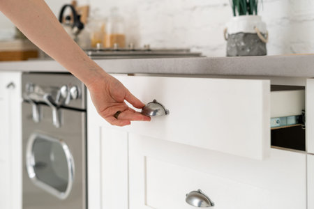 Cropped view of woman open white wooden drawer, standing in kitchen at modern house with new furniture and cozy interiorの写真素材