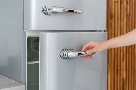 Cropped view of woman hand open fridge door, standing in contemporary kitchen with modern interior. Housewife using new refrigerator in dining roomの写真素材