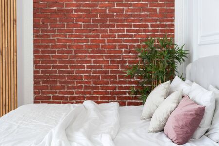Cozy bedroom with soft bed, pillows, blanket and white linen against red brick wall with copy space. Simple and comfortable interior at homeの写真素材