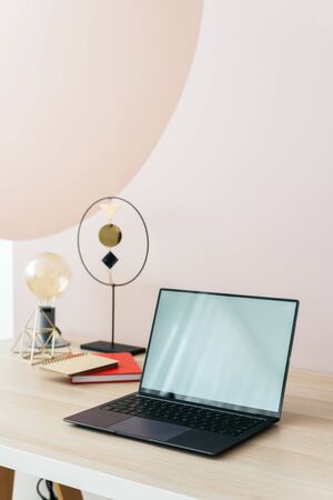 Vertical photo of contemporary interior in apartment with mockup display on modern laptop, still life decor on wooden table in remote work home officeの写真素材