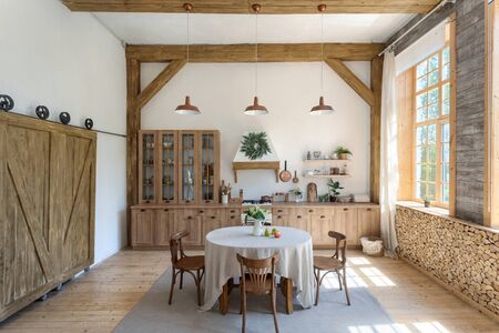 Facade of comfortable kitchen room with modern interior, extractor hood over gas stove, wooden furniture, flowers and tablecloth on dinner tableの写真素材