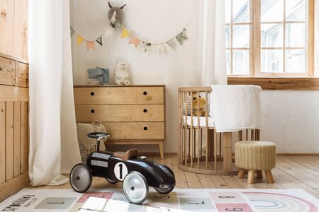 Comfortable kid bedroom in bohemian interior style with home decor, wooden chest of drawers, retro car toy and cozy sleeping baby placeの写真素材
