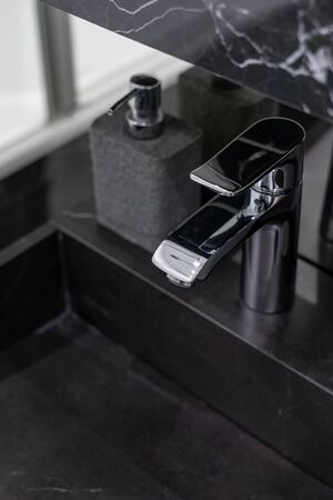 Vertical and selective focus of chrome faucet over black stone sink, soap dispenser on side surface in modern bathroom with contemporary interior designの写真素材