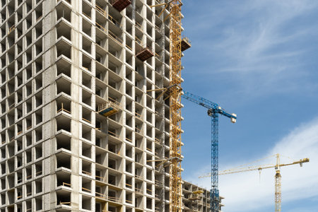 Modern building under construction with scaffolding equipment and tower crane equipment against blue...