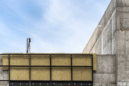 Architecture concept. Element of modern building under construction with rock wool insulation on exterior and copy space on concrete wall, against blue sky on backgroundの写真素材