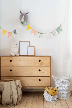 Vertical photo of cozy child bedroom with authentic interior design, flags on wall, home decor in wicker basket, toys on wooden chest of drawersの写真素材