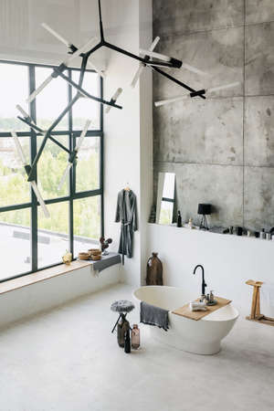 Vertical and high angle view of contemporary house interior at white bathroom with clean dry towels on wooden shelf. Modern empty bath, cotton bathrobe and home decor with copy space on concrete floorの写真素材
