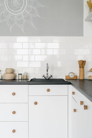 Vertical photo of white modern house with kitchen in tiled wall, drawers over cupboards, utensils...