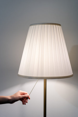 Vertical photo of woman hand pulling chain on white flooring lamp. Element of modern living room...