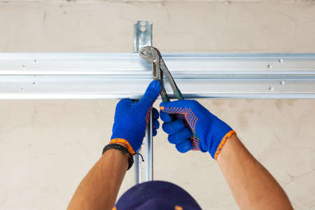 Concept of replacement details. Cropped view of professional worker using hand tool and install metal rail on garage door system in new house under constructionの写真素材