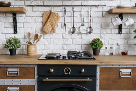 Gas stove, built in oven equipment, kitchenware supplies and houseplant in flower pot. Wooden kitchen in apartment with modern interior and new furnitureの写真素材