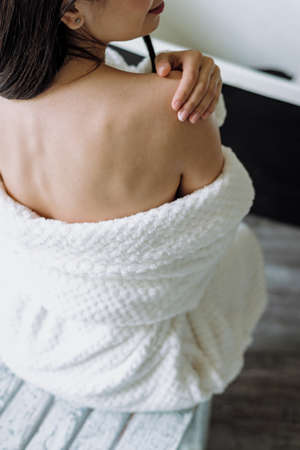 High angle cropped view of woman apply cream on skin, using natural pampering and moisturizing cosmetics. Back and vertical photo of young adult female in bathrobe, spending morning at bathroomの写真素材