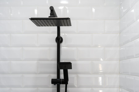 Close up of black shower head on holder against tiled wall on background. Concept of white bathroom...