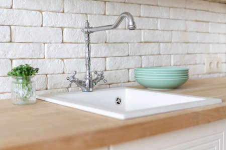 Selective focus on plates and microgreen plants on wooden countertop surface near sink and water tap on white kitchen in apartment with modern interiorの写真素材