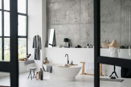 Modern bathroom with contemporary interior design, white ceramic bathtub, house decor, fresh clean towels against grey copy space and concrete wallの写真素材