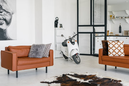 Comfortable living room with modern interior design, pillows on leather armchair, scooter at...